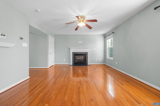 unfurnished living room with light wood finished floors, baseboards, ceiling fan, and a fireplace with flush hearth