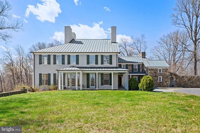  - rear view of property with a chimney, a standing seam roof, stucco siding, and a lawn