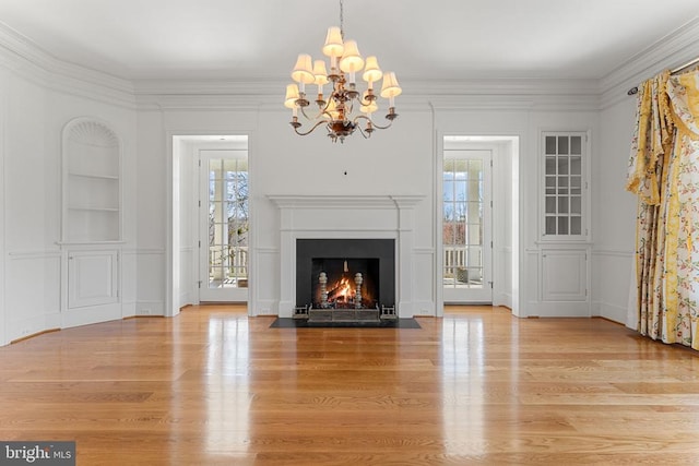  - unfurnished living room with built in shelves, light wood-style floors, a chandelier, a fireplace with flush hearth, and ornamental molding