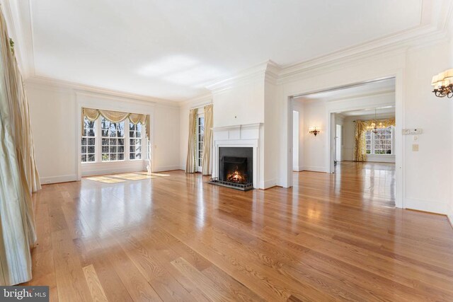  - unfurnished living room featuring a chandelier, healthy amount of natural light, a fireplace with flush hearth, ornamental molding, and wood finished floors