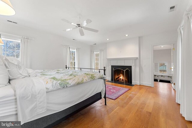  - bedroom featuring multiple windows, light wood-style flooring, recessed lighting, ceiling fan, and a fireplace with flush hearth
