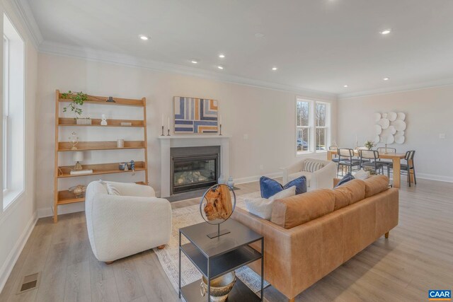 living area featuring a fireplace with flush hearth, visible vents, light wood-style flooring, and ornamental molding