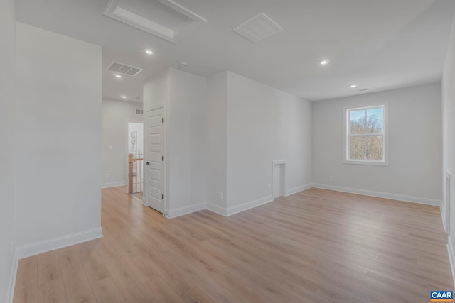 unfurnished room featuring attic access, light wood-type flooring, visible vents, baseboards, and recessed lighting