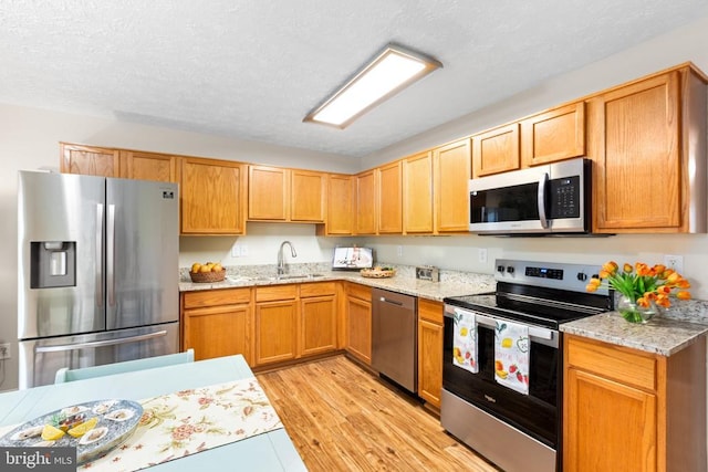 2912 Broyhill Ct, Fredericksburg, VA 22408 - kitchen with appliances with stainless steel finishes, a sink, a textured ceiling, light wood finished floors, and light stone counters