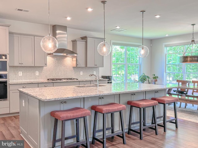 8525 Laroque Run Dr, Fredericksburg, VA 22407 - kitchen featuring wall chimney range hood, a sink, gray cabinetry, tasteful backsplash, and light wood-type flooring