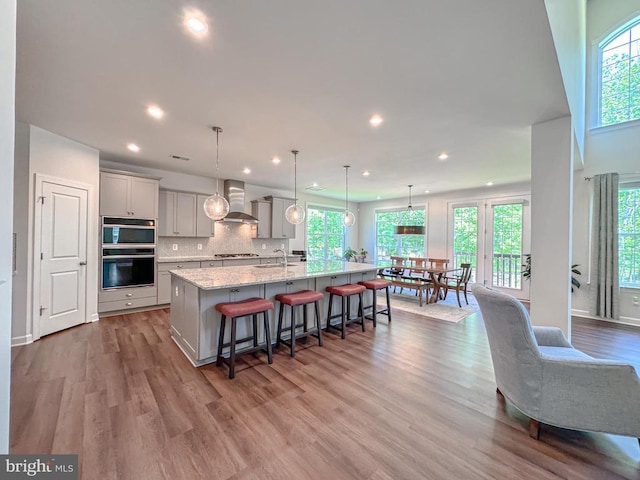 8525 Laroque Run Dr, Fredericksburg, VA 22407 - kitchen with a sink, gray cabinets, a breakfast bar area, a large island with sink, and wall chimney exhaust hood