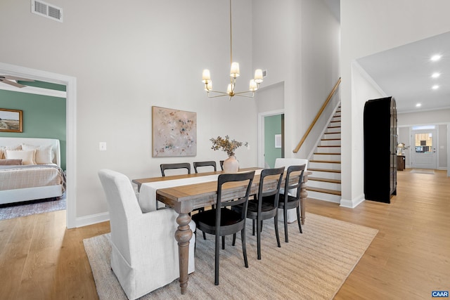 dining room featuring light wood finished floors, a high ceiling, visible vents, baseboards, and stairway