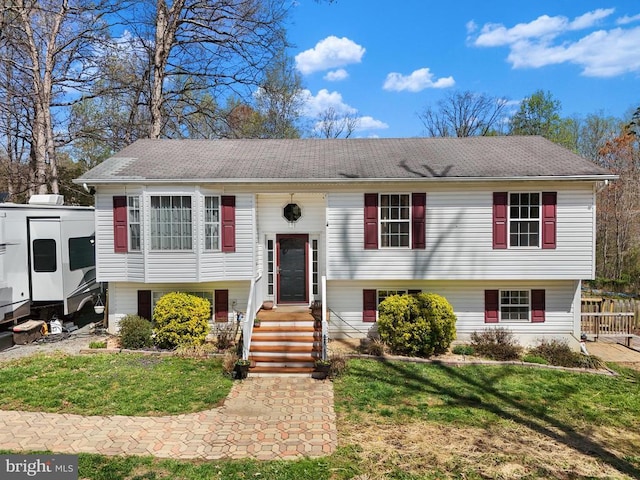 raised ranch with a front yard and roof with shingles