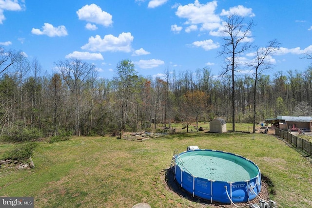 view of yard featuring a storage unit, an outdoor structure, an outdoor pool, and a wooded view
