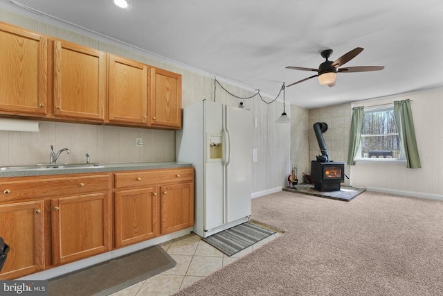 kitchen featuring white refrigerator with ice dispenser, a sink, a wood stove, a ceiling fan, and brown cabinets