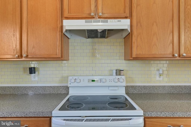 kitchen with under cabinet range hood, white range with electric stovetop, backsplash, and dark countertops