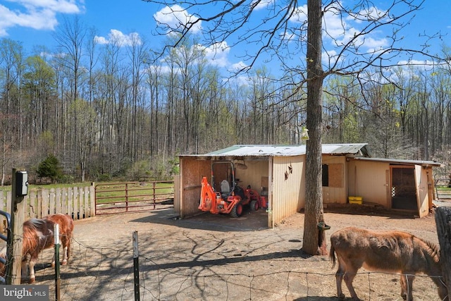 view of outdoor structure with fence, a wooded view, and a carport