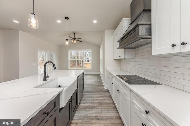 kitchen featuring custom range hood, a sink, light wood finished floors, vaulted ceiling, and black electric stovetop