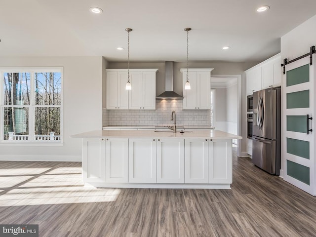 kitchen featuring wall chimney exhaust hood, stainless steel refrigerator with ice dispenser, a barn door, light countertops, and dark wood finished floors