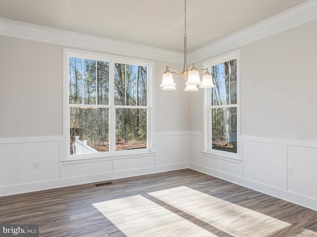 unfurnished dining area with a chandelier, wainscoting, wood finished floors, and a decorative wall