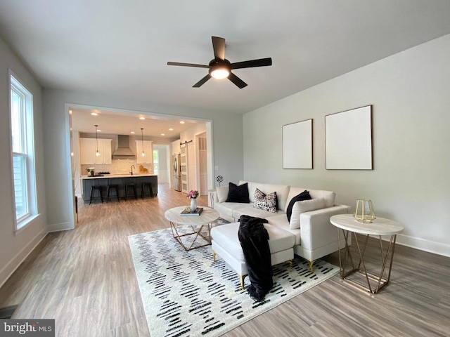 living area featuring wood finished floors, baseboards, a ceiling fan, and plenty of natural light