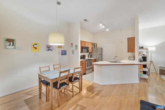kitchen featuring light wood finished floors, a sink, track lighting, a peninsula, and appliances with stainless steel finishes