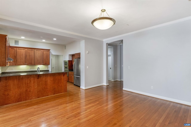 112 5th St SE Unit 3D, Charlottesville, VA 22902 - kitchen featuring appliances with stainless steel finishes, a peninsula, brown cabinets, light wood-style flooring, and baseboards
