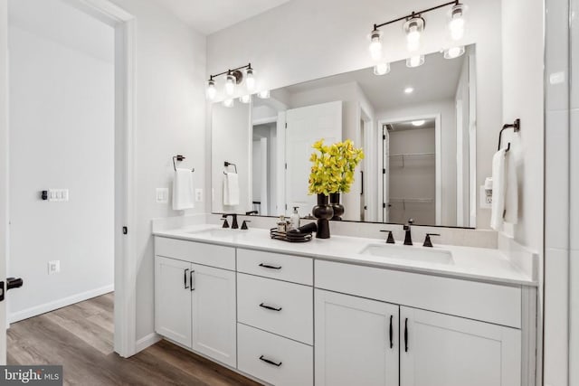 full bathroom with wood finished floors, double vanity, a walk in closet, and baseboards