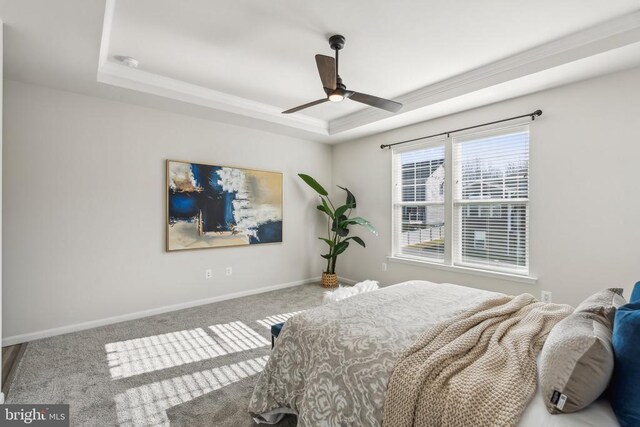 bedroom featuring a raised ceiling, crown molding, carpet floors, baseboards, and ceiling fan