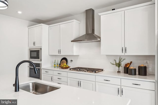 kitchen featuring wall chimney exhaust hood, stainless steel gas cooktop, a sink, black microwave, and light countertops