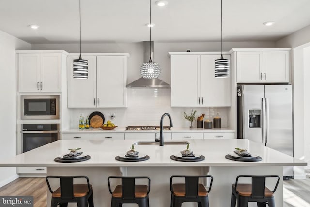 kitchen with stainless steel appliances, wall chimney exhaust hood, a sink, light countertops, and a breakfast bar