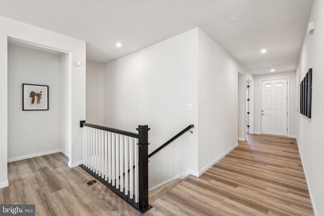 hallway with an upstairs landing, recessed lighting, wood finished floors, and baseboards