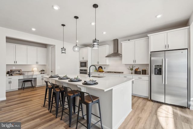 kitchen with appliances with stainless steel finishes, wall chimney range hood, a sink, light wood finished floors, and a kitchen bar