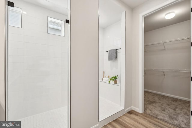 full bath featuring a tile shower, wood finished floors, a spacious closet, and baseboards