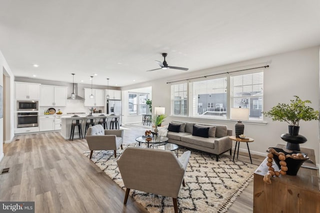 living room with light wood-type flooring, a ceiling fan, recessed lighting, and baseboards