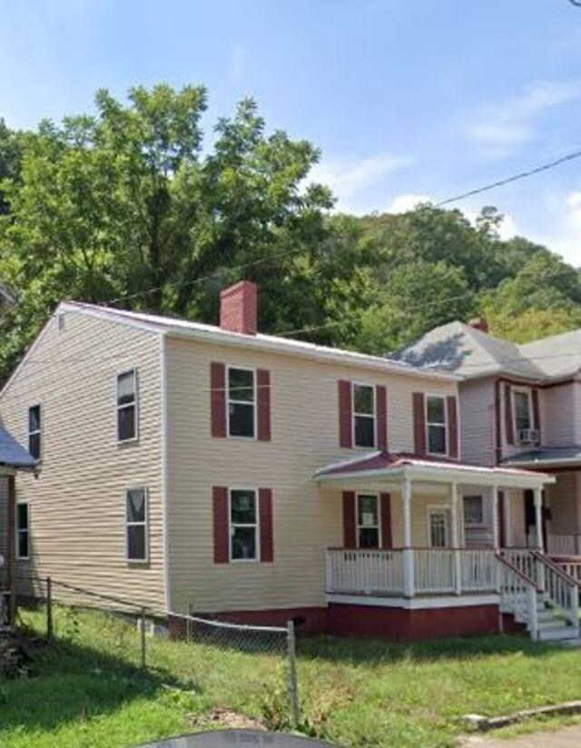 view of front of house with a porch, fence, a chimney, and a front yard