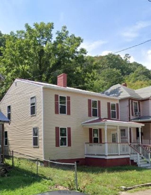 view of front of house with a porch, fence, a chimney, and a front yard