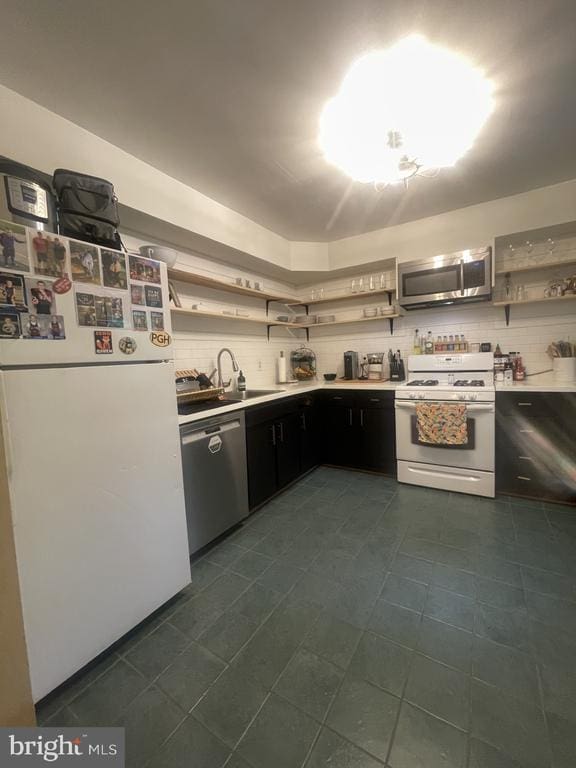 kitchen with appliances with stainless steel finishes, open shelves, dark cabinets, and light countertops