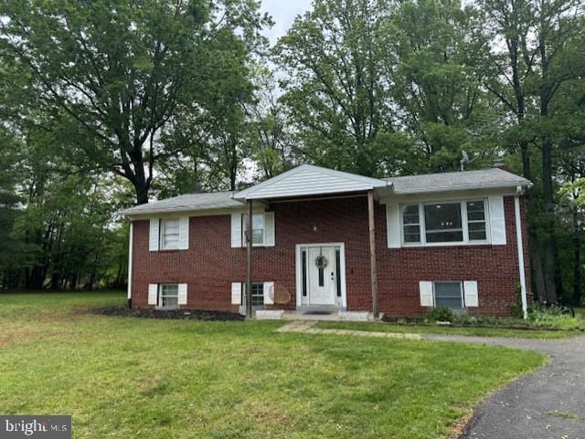 split foyer home featuring a front lawn, brick siding, and view of scattered trees