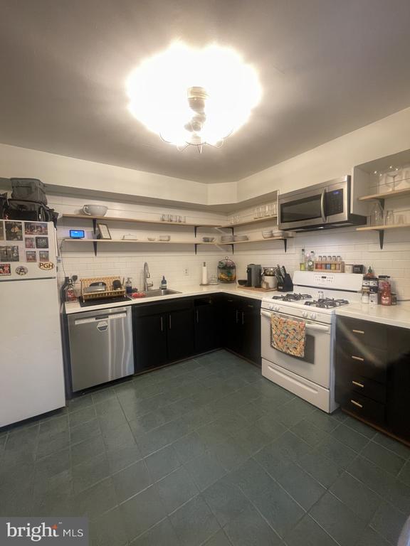 kitchen with open shelves, appliances with stainless steel finishes, a sink, dark cabinetry, and tasteful backsplash