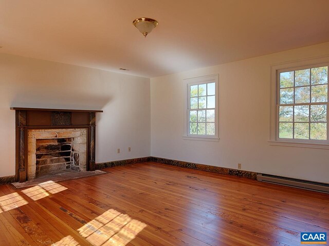 unfurnished living room with a baseboard heating unit, a stone fireplace, and wood-type flooring