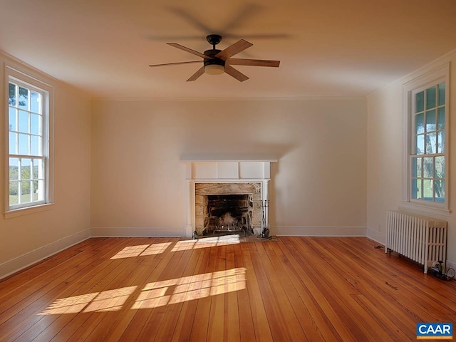 unfurnished living room featuring crown molding, light hardwood / wood-style flooring, ceiling fan, radiator heating unit, and a stone fireplace