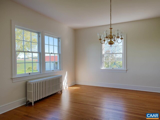 unfurnished dining area featuring an inviting chandelier, radiator heating unit, wood-type flooring, and plenty of natural light