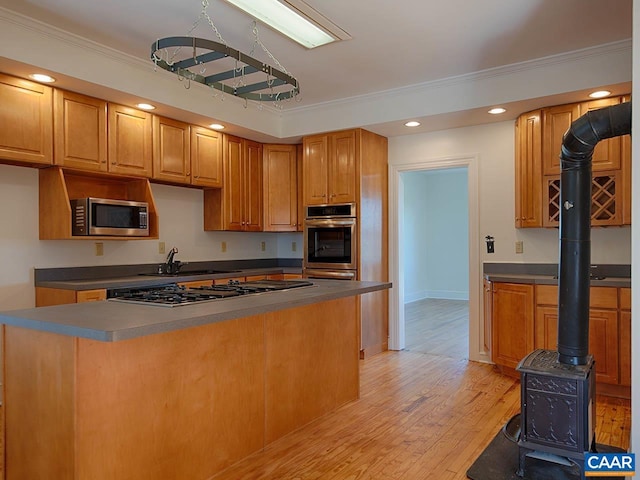 kitchen featuring sink, crown molding, appliances with stainless steel finishes, light hardwood / wood-style floors, and a wood stove