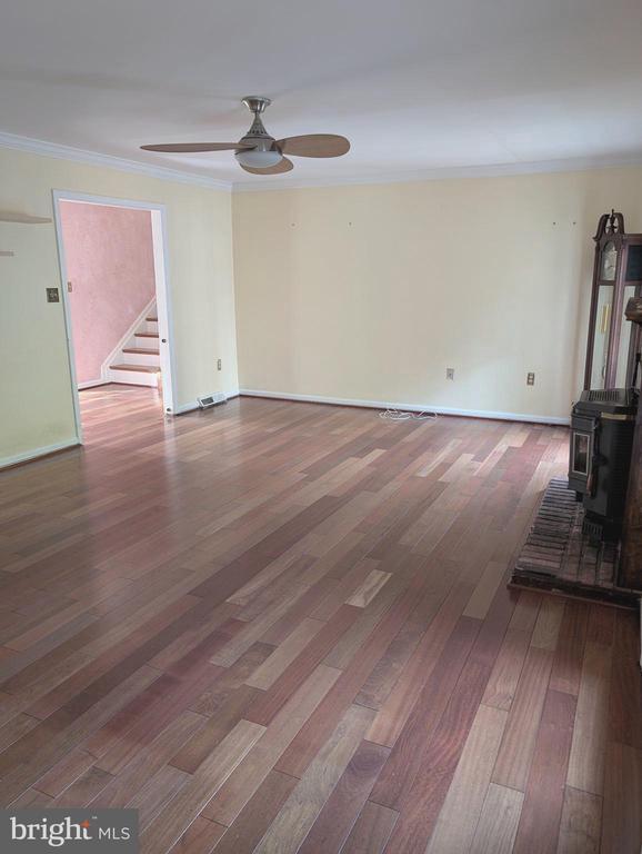  - unfurnished living room featuring a wood stove, a ceiling fan, crown molding, stairs, and wood finished floors