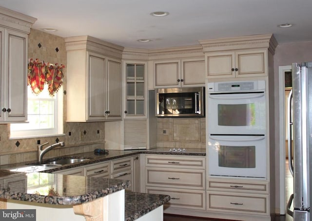 - kitchen with cream cabinets, stainless steel appliances, a sink, and dark stone countertops