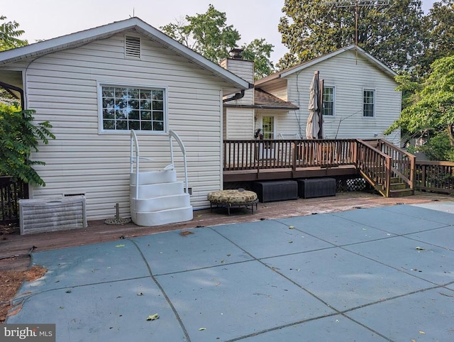  - back of house featuring a wooden deck, a chimney, a swimming pool, and a patio
