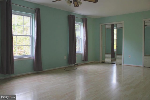  - unfurnished bedroom featuring wood finished floors, multiple closets, baseboards, and ceiling fan