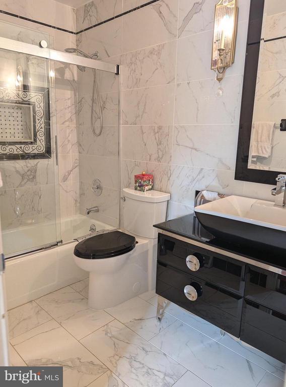  - bathroom featuring marble look tiles, enclosed tub / shower combo, toilet, vanity, and tile walls