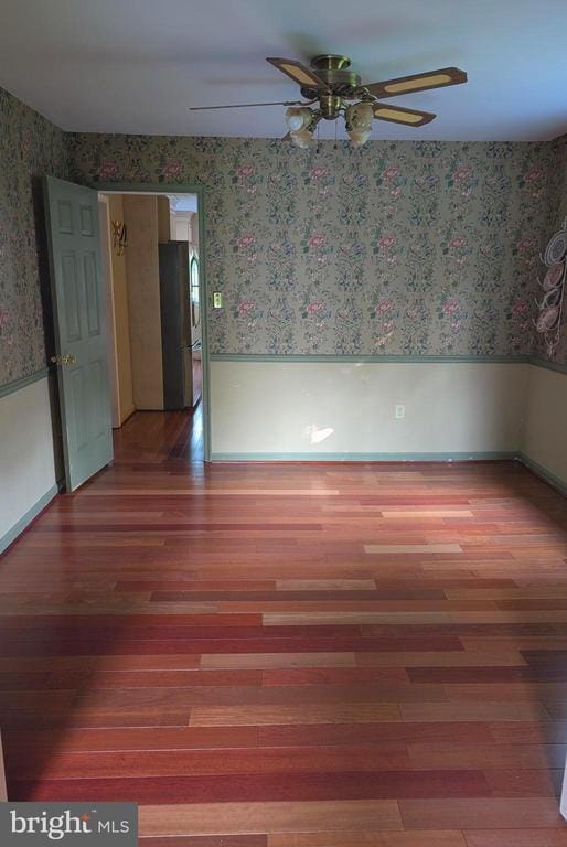  - spare room with wallpapered walls, a ceiling fan, wood finished floors, and baseboards