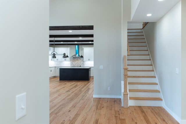 interior space with wall chimney exhaust hood, a center island, light hardwood / wood-style flooring, white cabinets, and backsplash