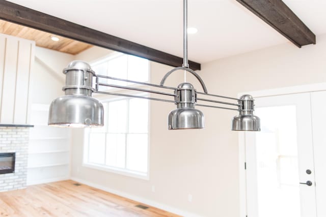 room details featuring beamed ceiling, wood-type flooring, and a brick fireplace