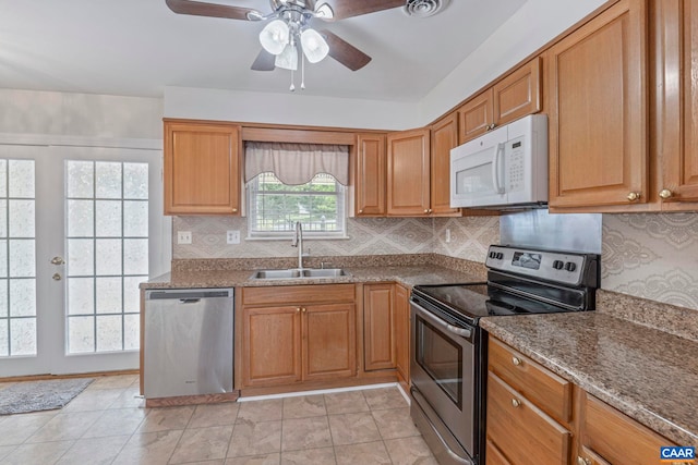 kitchen featuring appliances with stainless steel finishes, a sink, a ceiling fan, decorative backsplash, and brown cabinetry