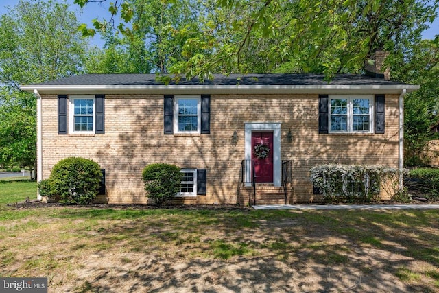 split foyer home featuring a chimney, brick siding, and a front lawn