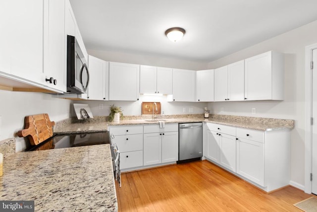 kitchen featuring appliances with stainless steel finishes, white cabinets, light wood-style floors, and a sink